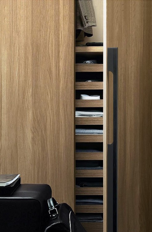 Czarny matowy uchwyt meblowy Vista zamontowany pionowo na wysokiej drewnianej garderobie