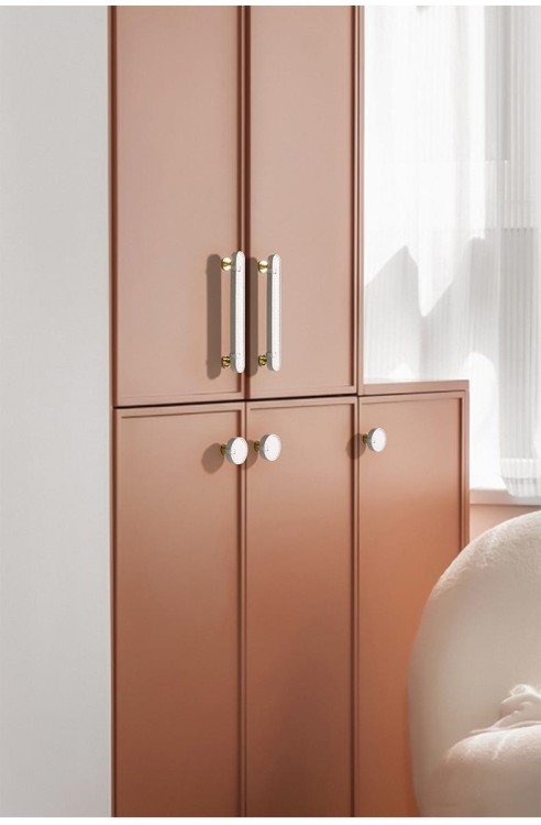 Białe skórzane uchwyty meblowe Museo zamontowane na frontach wysokiej szafy w sypialni