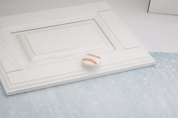 Gałka meblowa w kształcie piłki do baseballu zamontowana na białym froncie szuflady